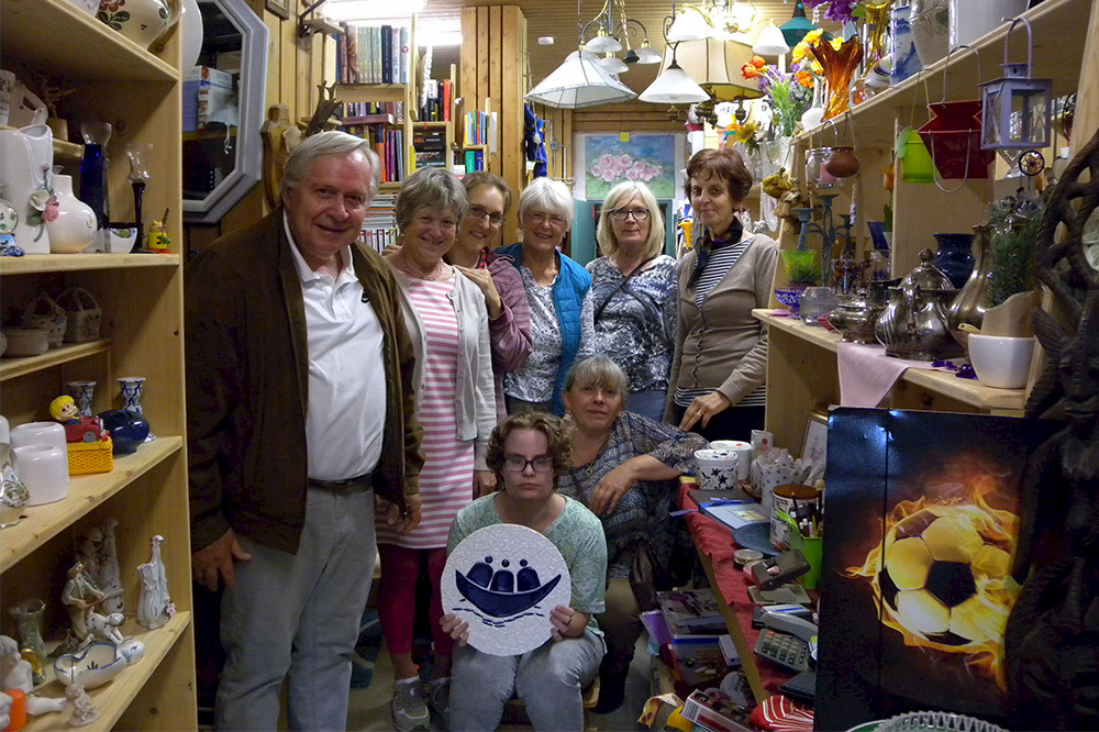 Bild zeigt Menschen in einem Geschäft. Sie halten das Logo der Arche.